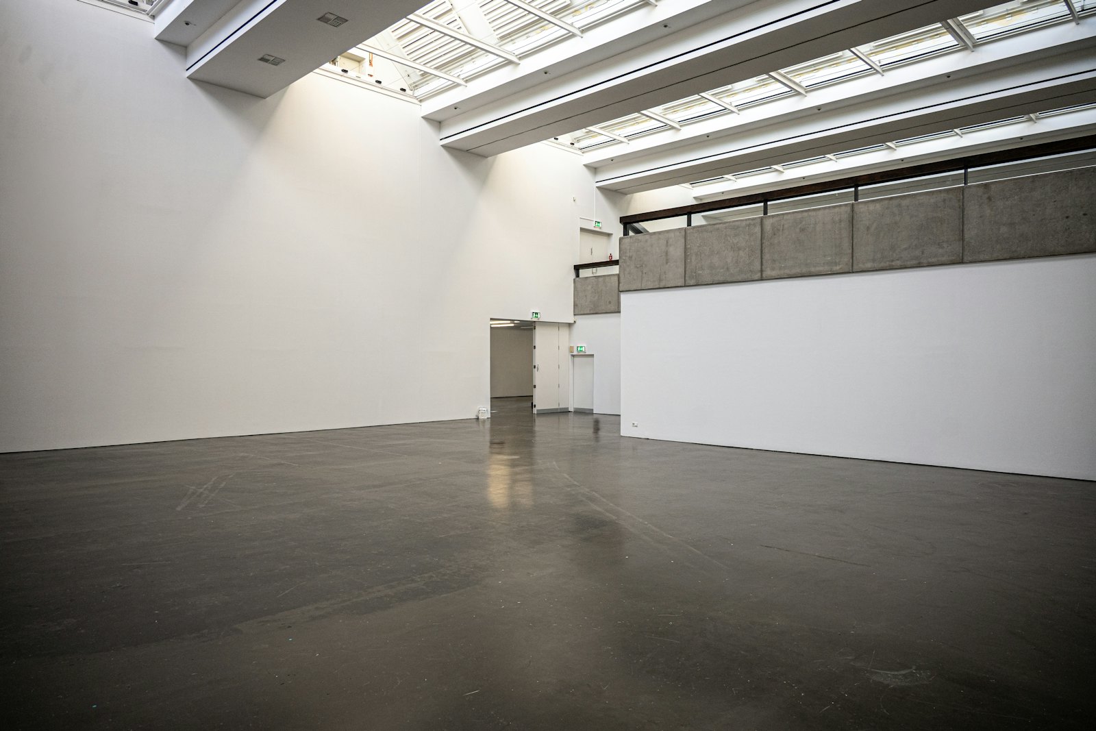 Empty gallery space with a dark polished concrete floor, white walls and a skylit ceiling