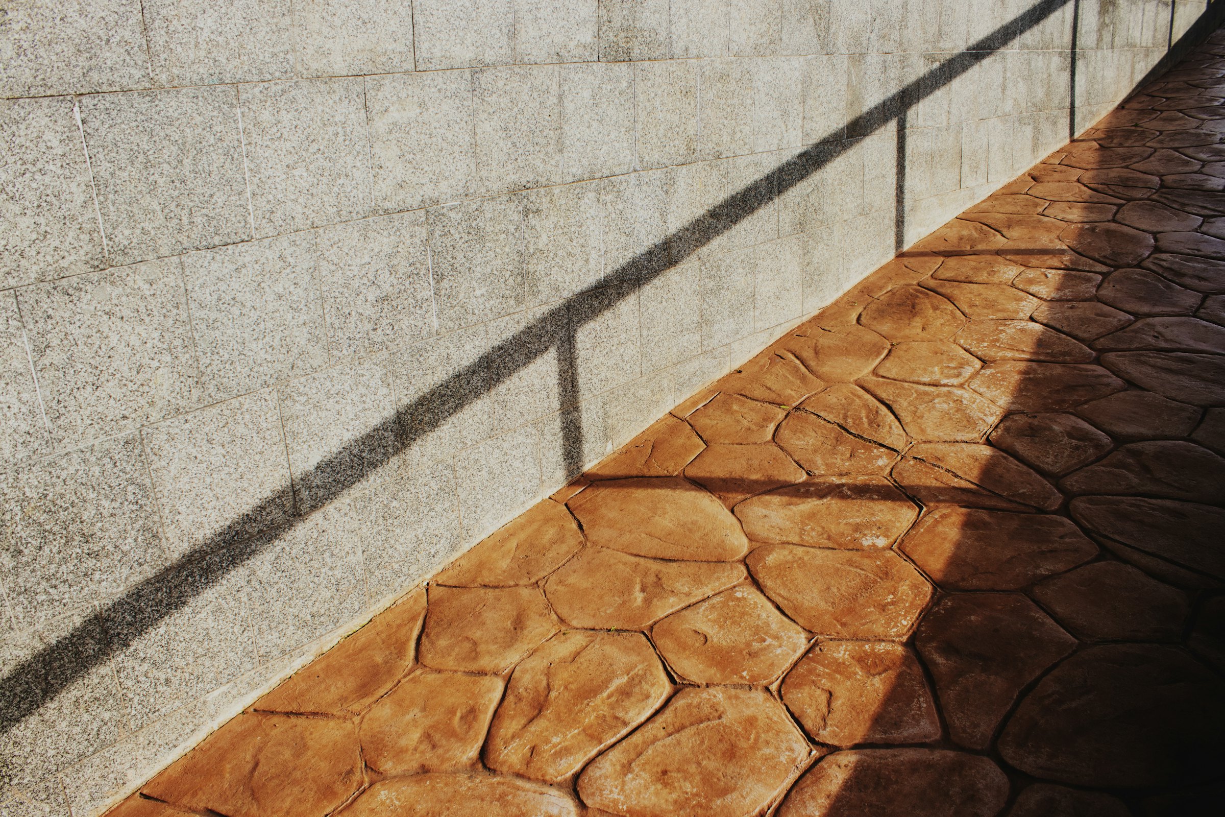 Orange-toned stone-pattern (stamped-concrete style) walkway beside a textured block wall, half in shadow