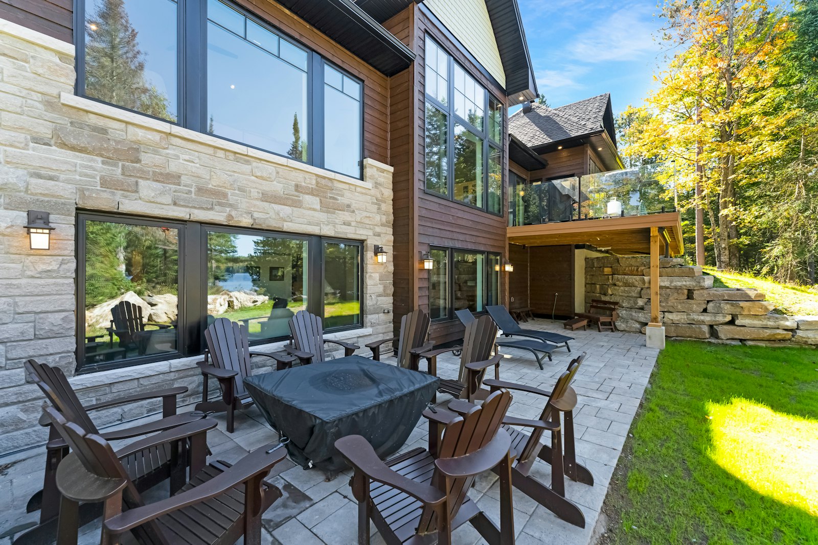 Stone-paver patio with Adirondack chairs around a fire table beside a stone-clad home