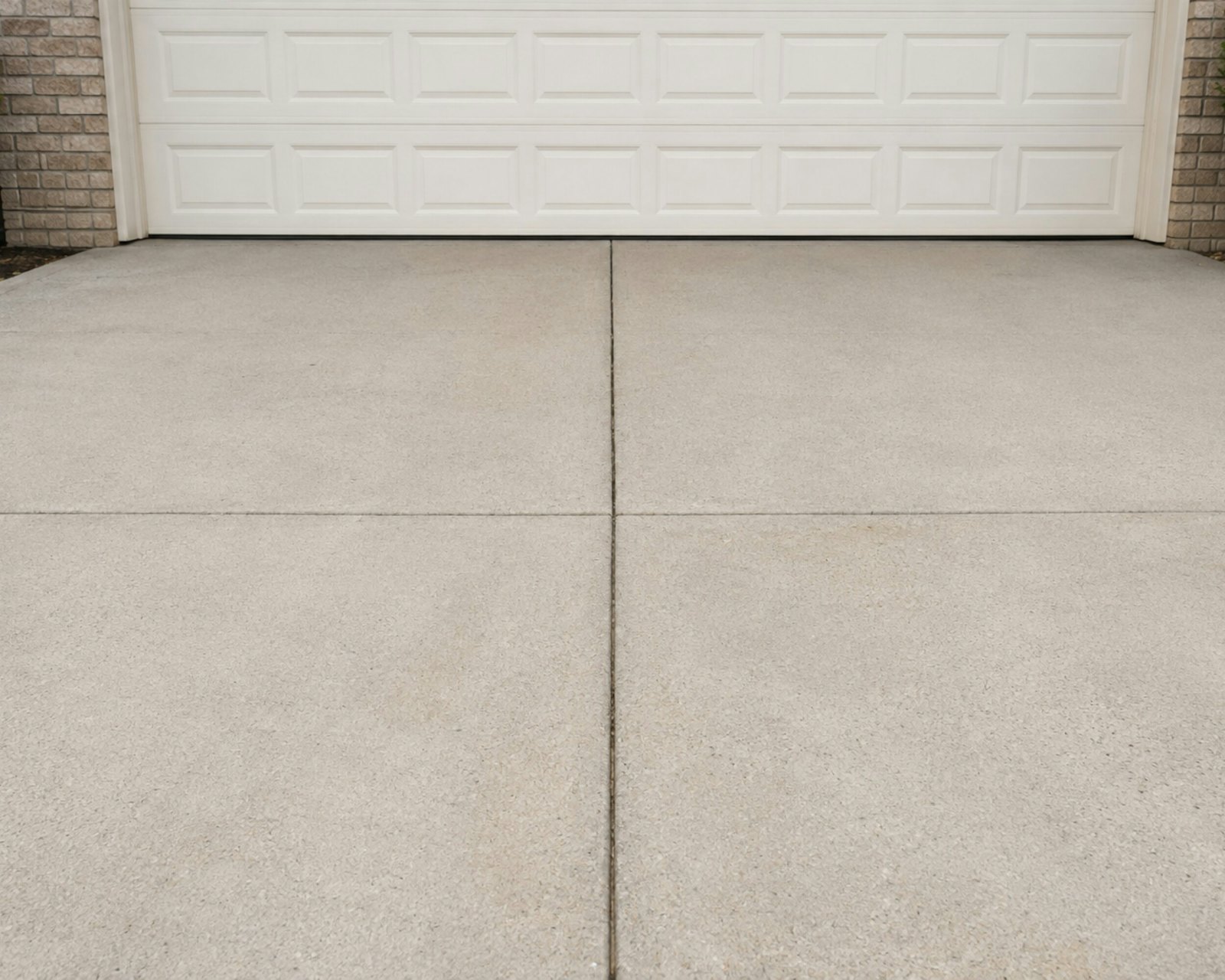Close-up of a broom-finished concrete driveway with control joints in front of a white garage door